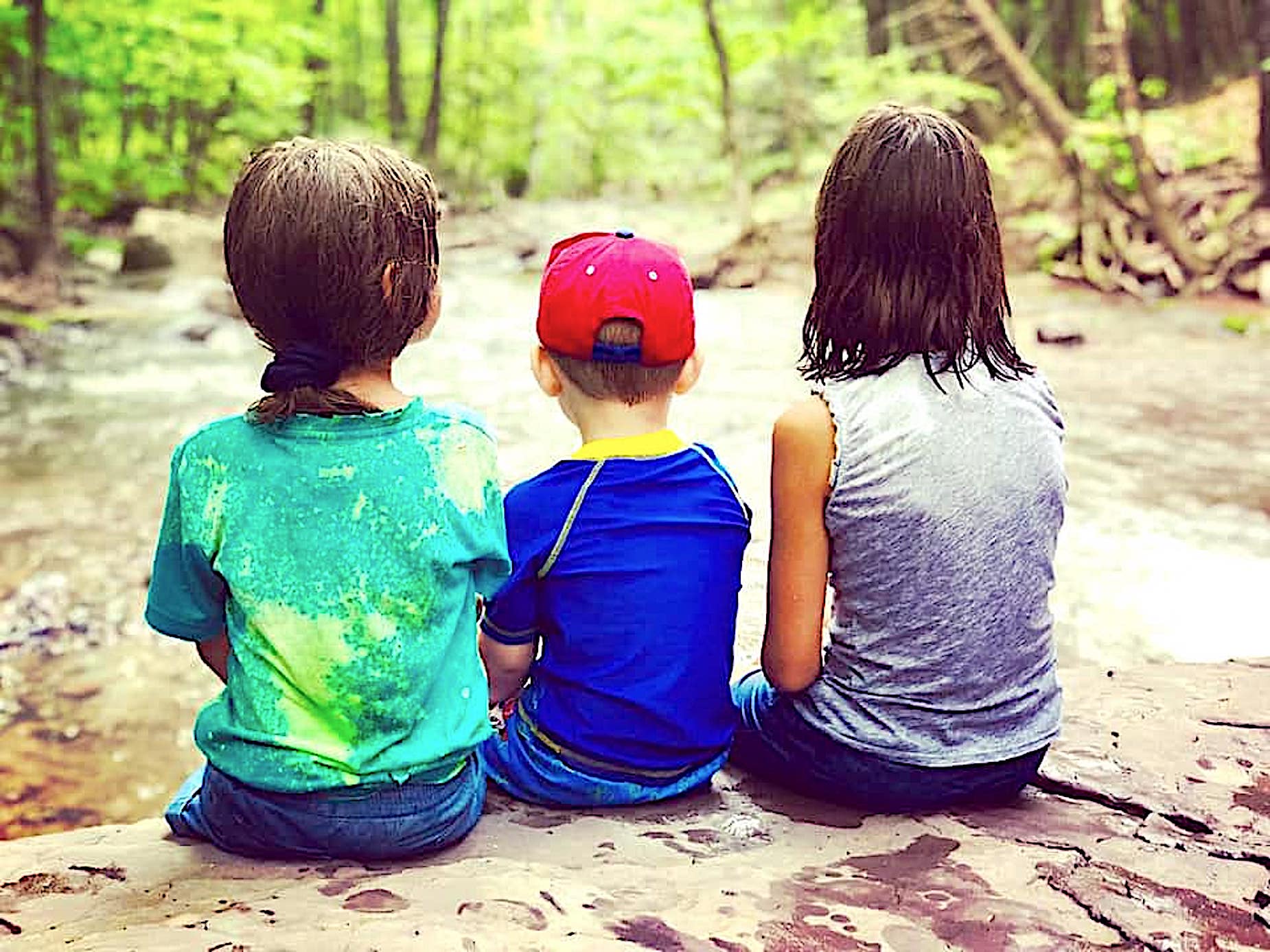 Three kids sitting next to a stream.