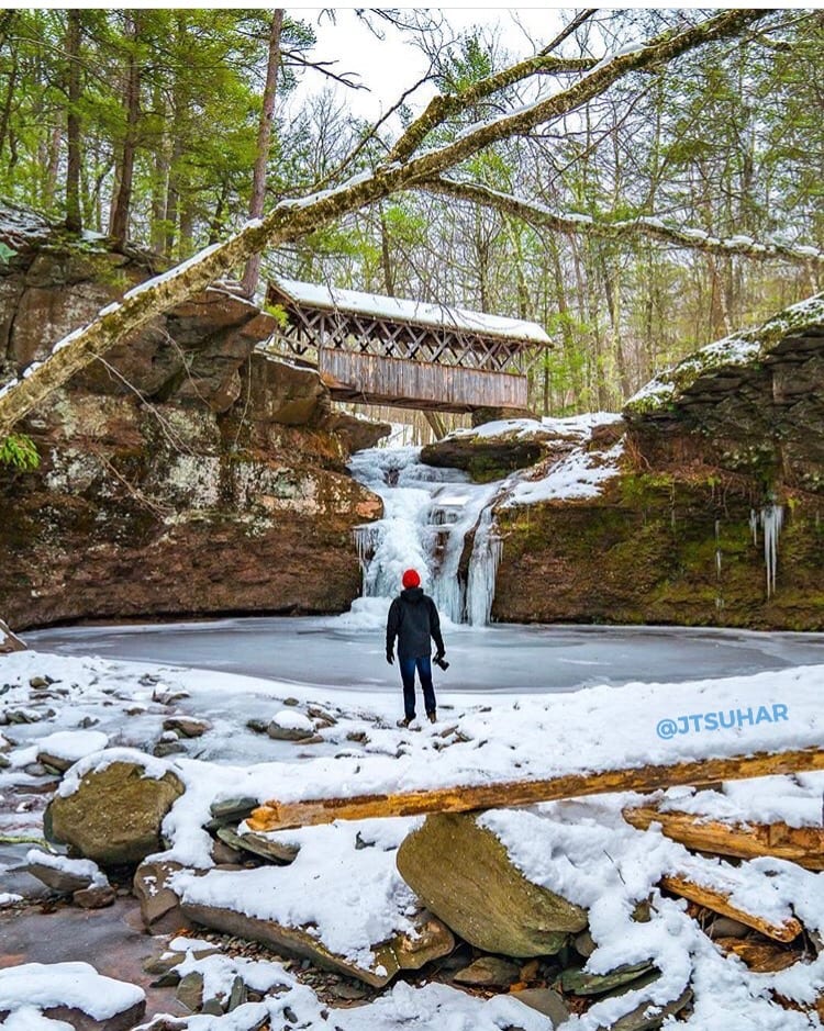 Person looking at frozen waterfalls with covered bridge